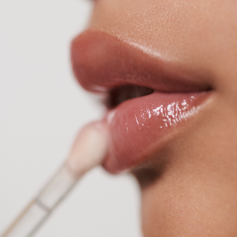 A female applying La Mer The Lip Volumizer to her lips. The hydrating lip serum glides smoothly, offering a glossy finish and fuller appearance.