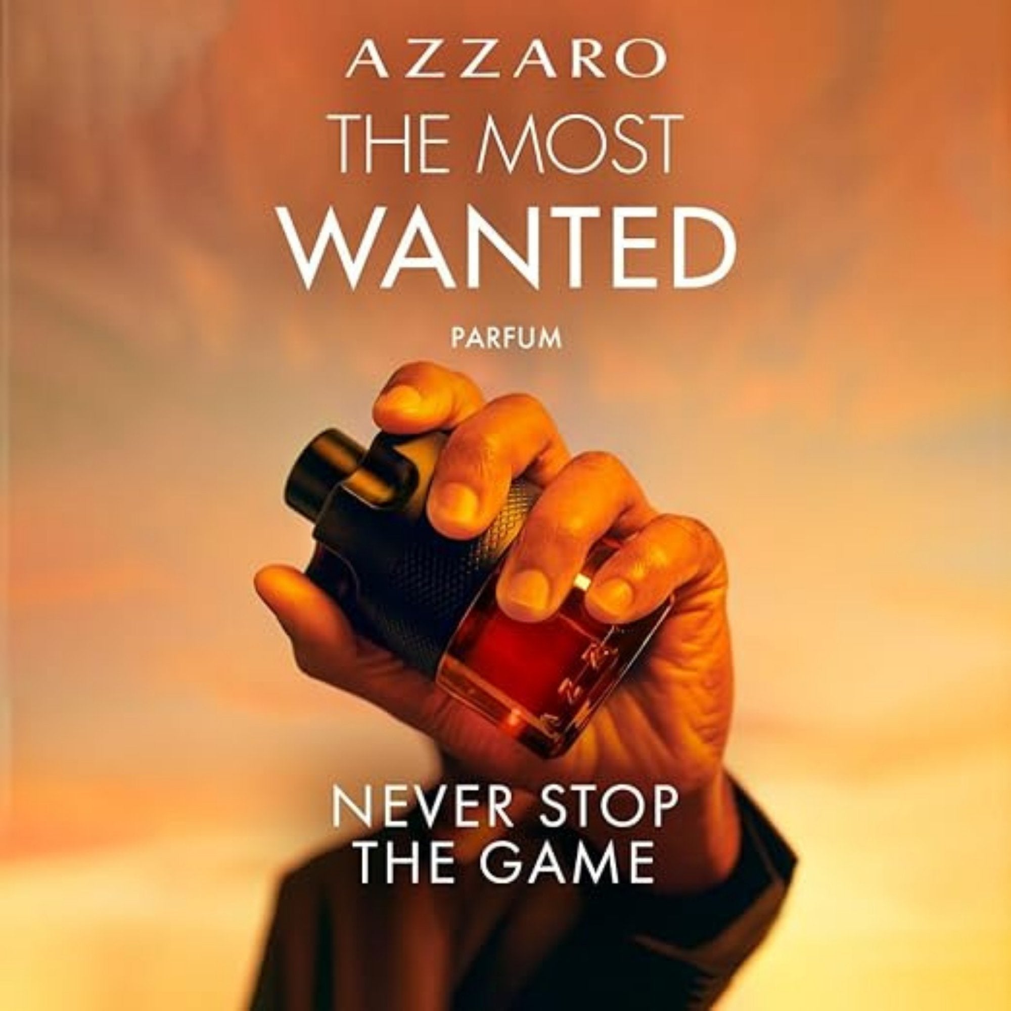 Hand holding a perfume bottle with 'Azzaro The Most Wanted' text on a warm-toned background